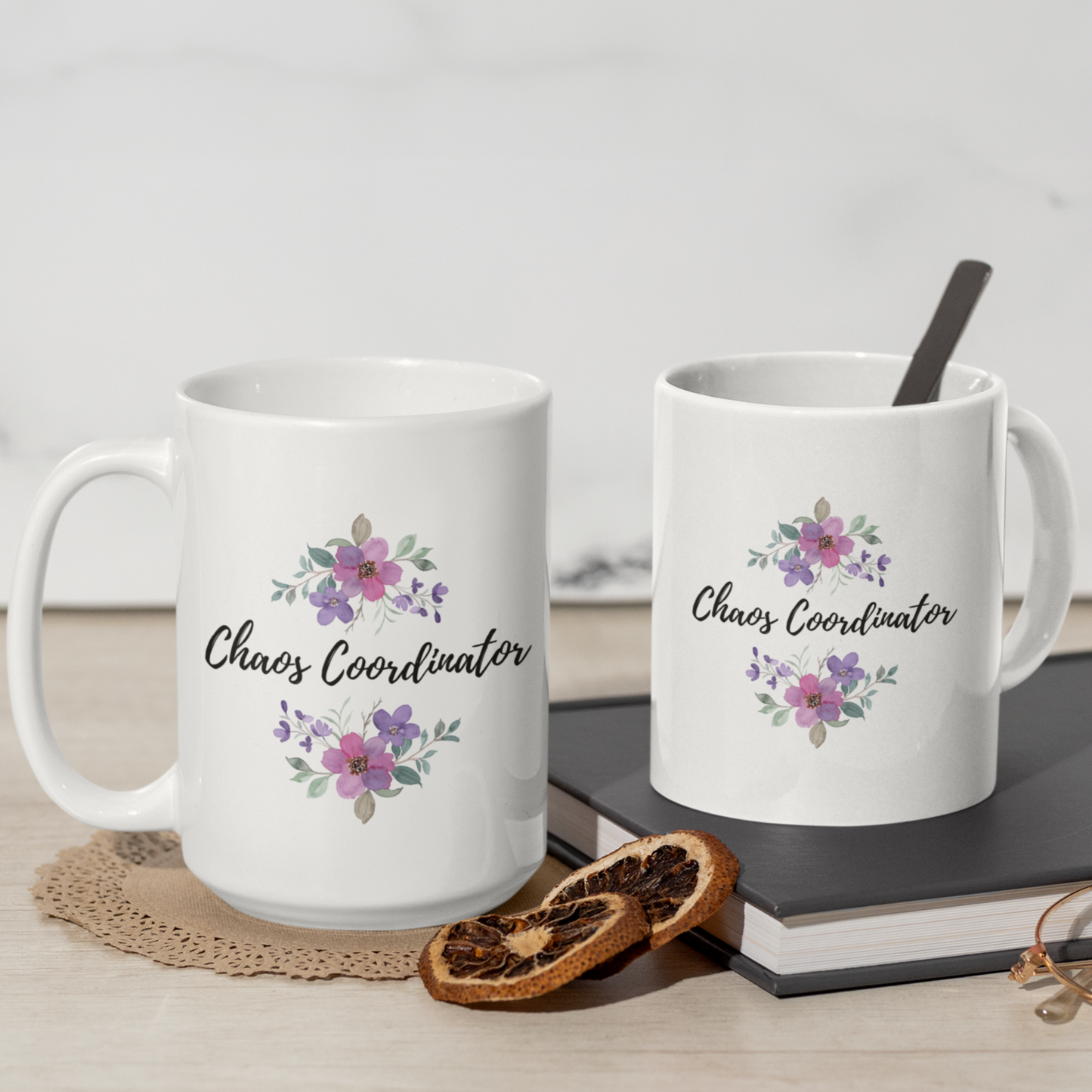 11 & 15 oz white ceramic coffee mug featuring the playful phrase “Chaos Coordinator” in stylish black script font centered on the front. Surrounding the text are delicate watercolor floral arrangements in shades of soft pink, lavender, and muted green leaves, adding a touch of elegance and charm. The mug has a smooth glossy finish and a sturdy C-shaped handle for easy grip.