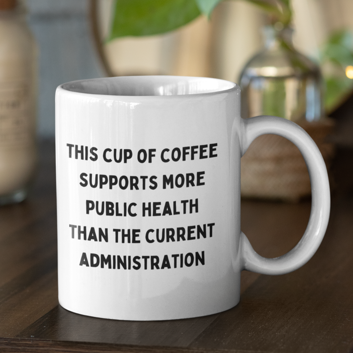 11 oz white ceramic coffee mug with handle, perfect for daily use at home or in the office. The mug features a bold, humorous political statement printed in all-caps black font: "THIS CUP OF COFFEE SUPPORTS MORE PUBLIC HEALTH THAN THE CURRENT ADMINISTRATION." The text is centered and covers most of the front surface, making it highly visible.