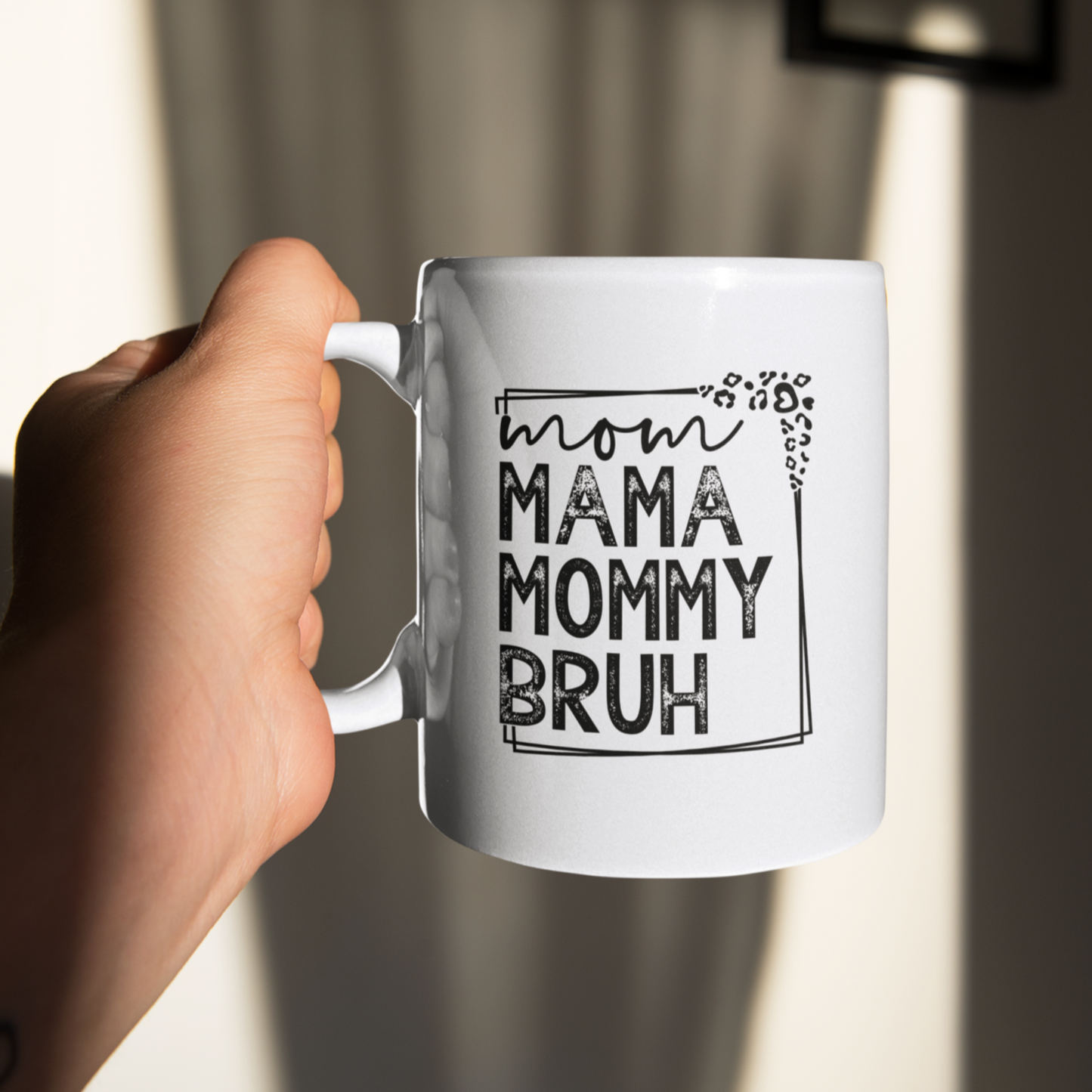 11 oz white mug displaying a playful design that reads "mom MAMA MOMMY BRUH" in black, framed with leopard print details. A funny gift for moms with a sense of humor.