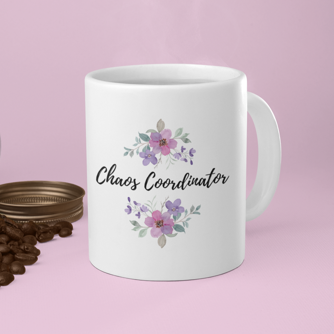 11 oz white ceramic coffee mug featuring the playful phrase “Chaos Coordinator” in stylish black script font centered on the front. Surrounding the text are delicate watercolor floral arrangements in shades of soft pink, lavender, and muted green leaves, adding a touch of elegance and charm. The mug has a smooth glossy finish and a sturdy C-shaped handle for easy grip.