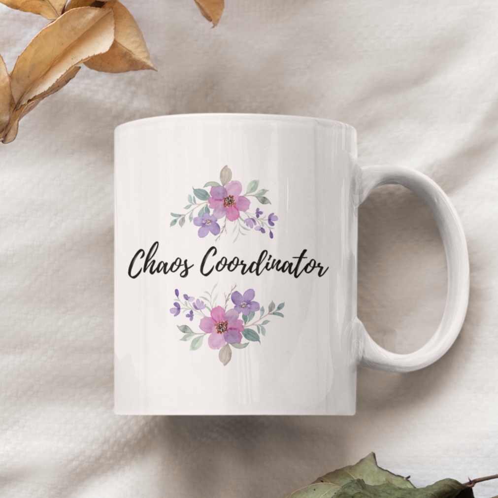 11 oz white ceramic coffee mug featuring the playful phrase “Chaos Coordinator” in stylish black script font centered on the front. Surrounding the text are delicate watercolor floral arrangements in shades of soft pink, lavender, and muted green leaves, adding a touch of elegance and charm. The mug has a smooth glossy finish and a sturdy C-shaped handle for easy grip.