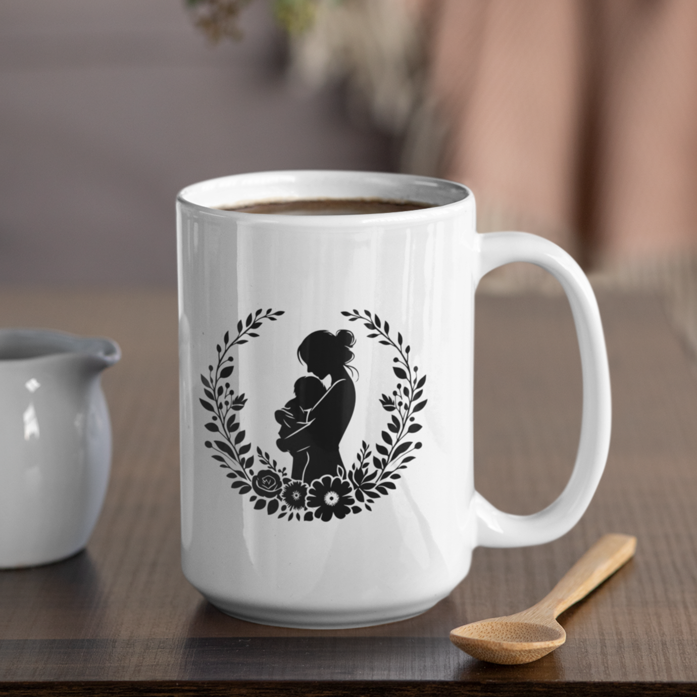 Charming white ceramic mug featuring a tender black silhouette of a mother cradling her baby, framed by a delicate floral wreath. This mug radiates love and comfort. Ideal for gifting to new moms, celebrating Mother’s Day, or honoring the beauty of motherhood. Durable, dishwasher and microwave safe—perfect for everyday coffee, tea, or cocoa moments.