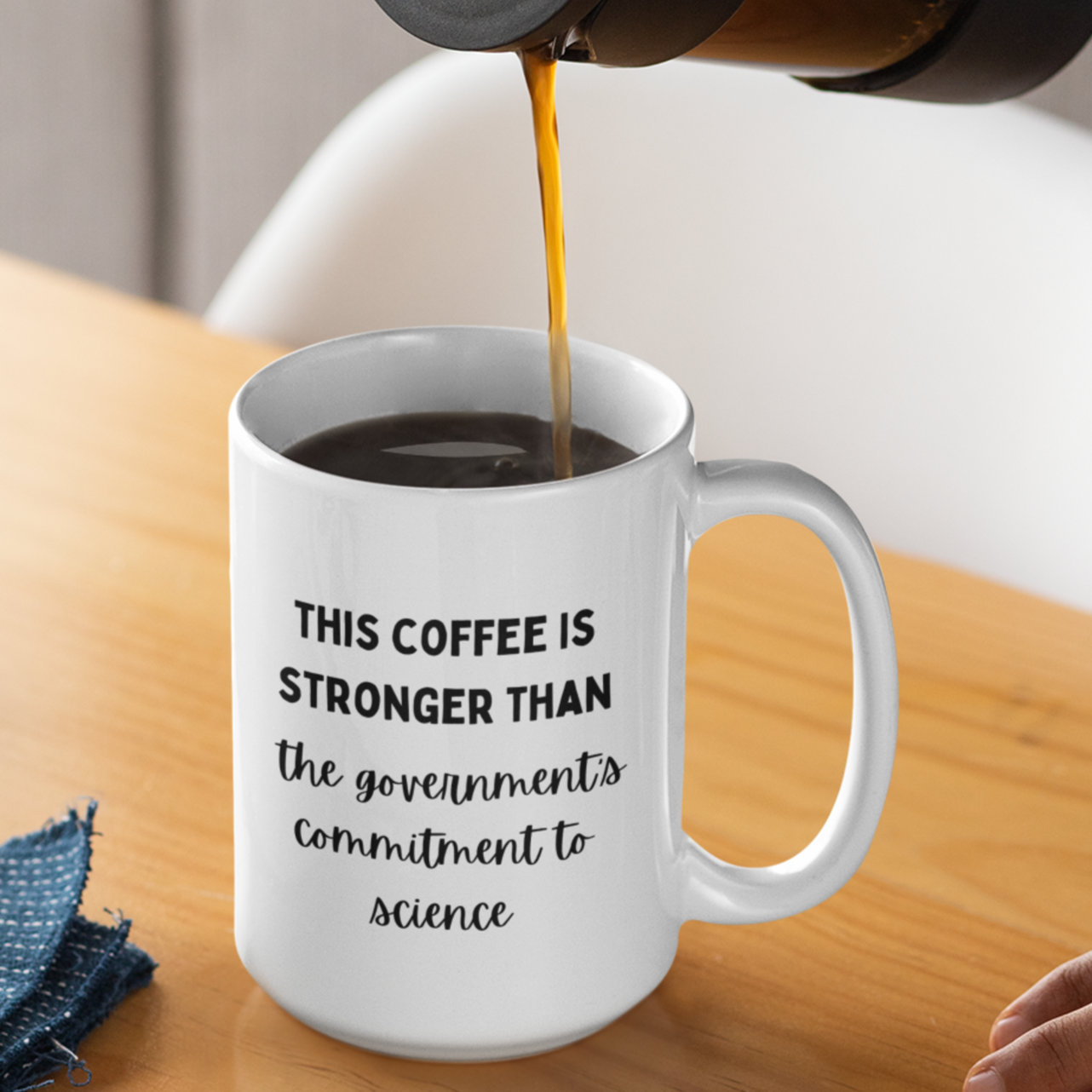 15 oz white ceramic coffee mug featuring a humorous and bold printed message in black typography. The text reads, "THIS COFFEE IS STRONGER THAN the government's commitment to science," with varying font styles—bold uppercase for emphasis and cursive script for a playful contrast.