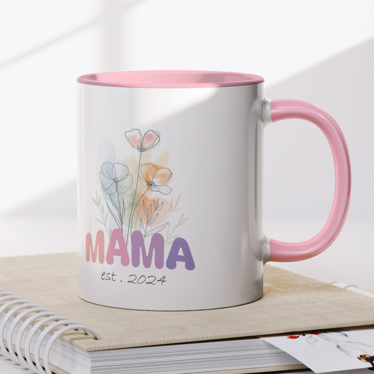Adorable 11 oz white ceramic coffee mug with a glossy finish, featuring a soft pink interior and matching pink handle. The design showcases a delicate watercolor floral bouquet above the word “MAMA” in cheerful gradient tones from pink to purple, with the text “est. 2024” in a stylish handwritten script below. This mug is a perfect gift for new moms celebrating their first Mother's Day or a sweet keepsake marking the beginning of their motherhood journey.