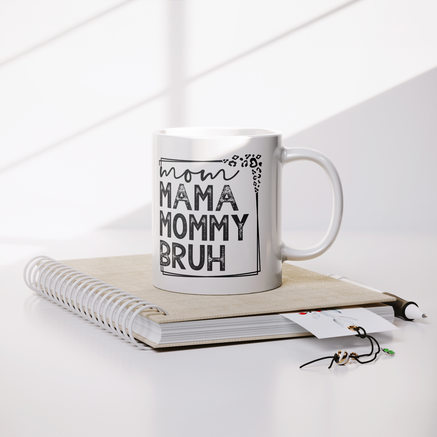 11 oz white mug displaying a playful design that reads "mom MAMA MOMMY BRUH" in black, framed with leopard print details. A funny gift for moms with a sense of humor.