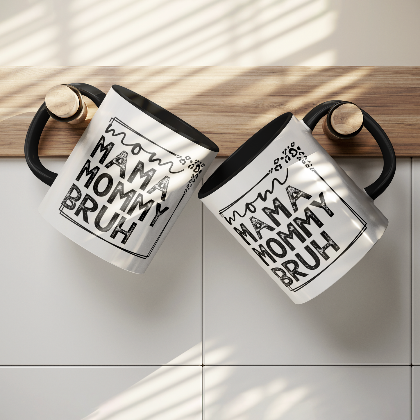 11 oz white ceramic mug with a black interior and handle. The mug features the black text "mom MAMA MOMMY BRUH" stacked vertically within a rectangular frame with leopard print accents. Dried citrus slices and small white flowers are arranged near the base of the mug.