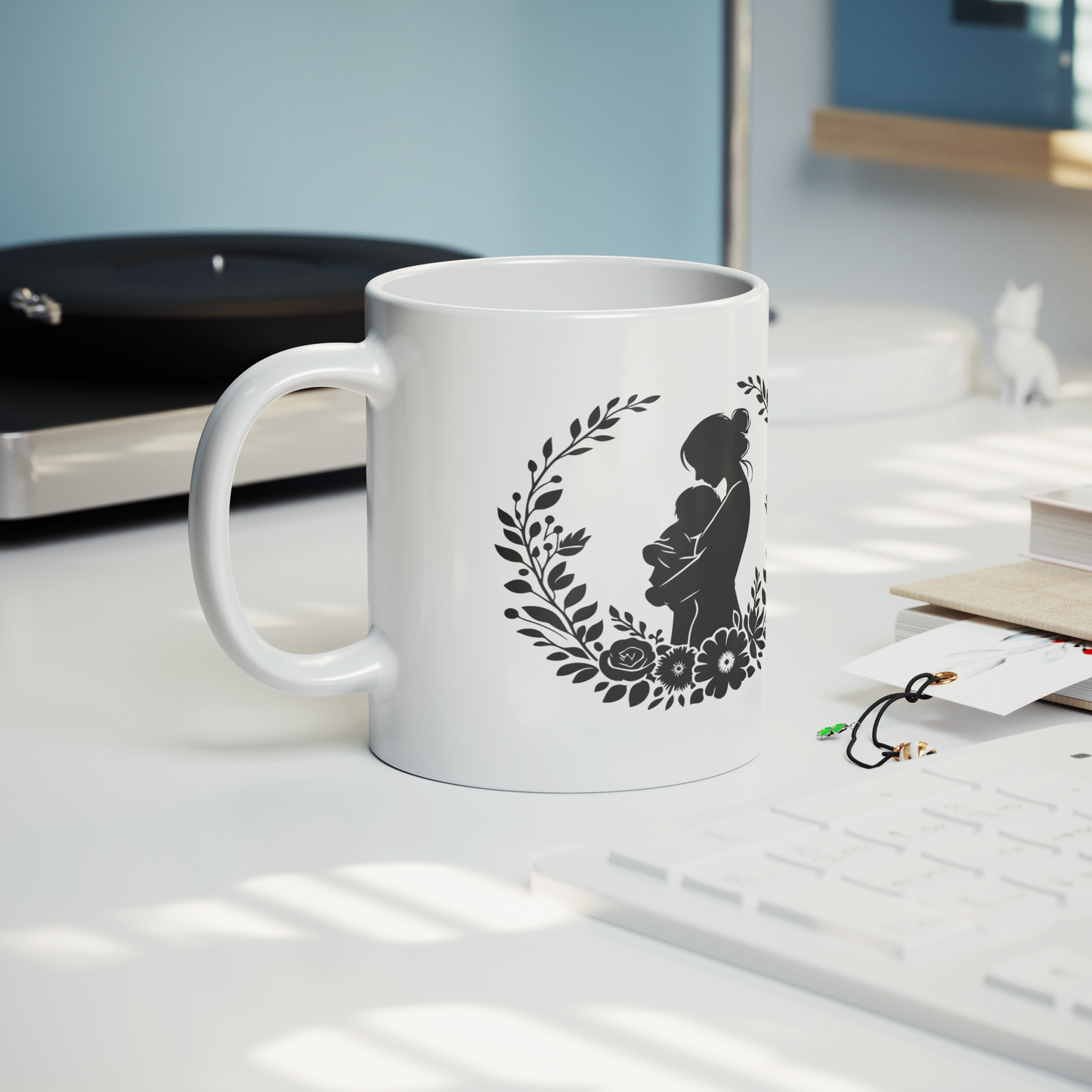 Charming white ceramic mug featuring a tender black silhouette of a mother cradling her baby, framed by a delicate floral wreath. This mug radiates love and comfort. Ideal for gifting to new moms, celebrating Mother’s Day, or honoring the beauty of motherhood. Durable, dishwasher and microwave safe—perfect for everyday coffee, tea, or cocoa moments.