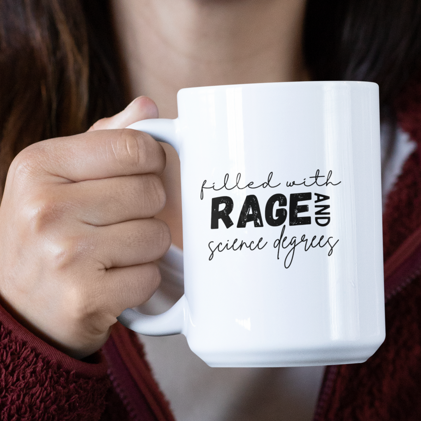 15 oz Close-up of a white ceramic coffee mug that features a bold and playful typography design that reads: "filled with RAGE AND science degrees." The words "RAGE AND" are in bold, uppercase letters, while the rest of the text is in a casual, handwritten script. Ideal for scientists, academics, or STEM enthusiasts.