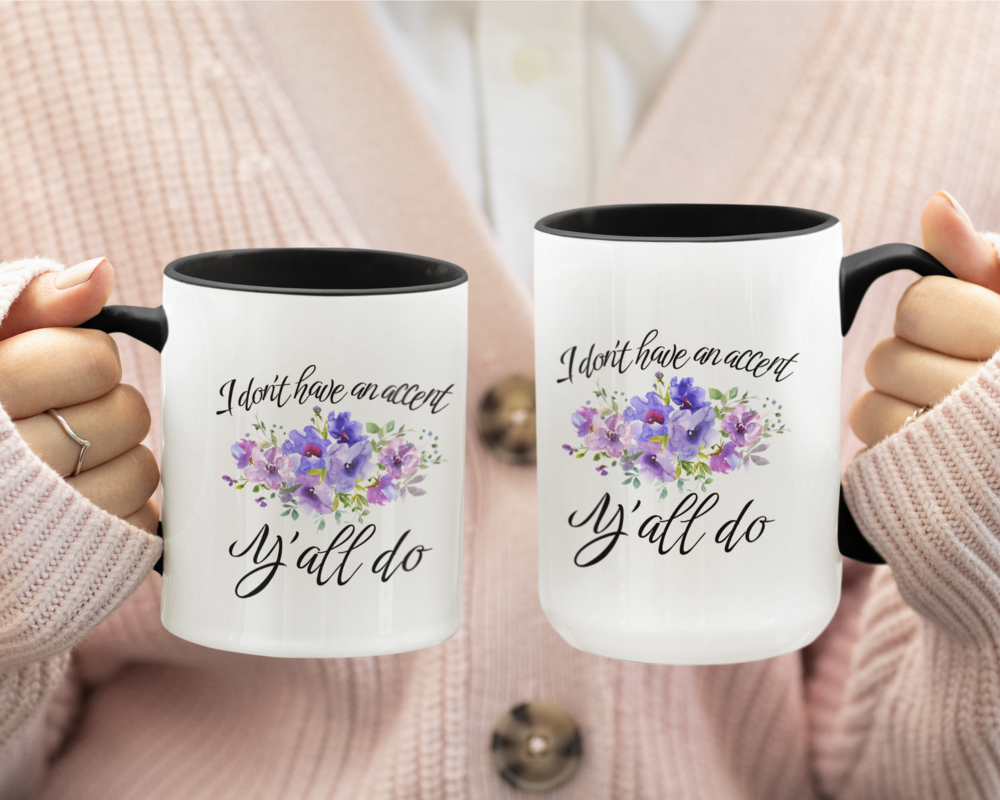 11 & 15 oz stylish ceramic coffee mug featuring a white glossy exterior with a contrasting black handle and black interior. The front of the mug displays elegant, cursive black text that reads, "I don't have an accent, y'all do," accented by a beautiful watercolor floral arrangement in shades of purple, lilac, and soft green.