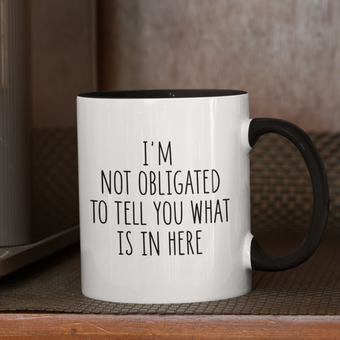 Simple yet impactful 11 oz white mug with black accents, featuring the witty statement "I'M NOT OBLIGATED TO TELL YOU WHAT IS IN HERE" in a clear black font. Perfect for those with a dry wit and a desire for a little beverage privacy.