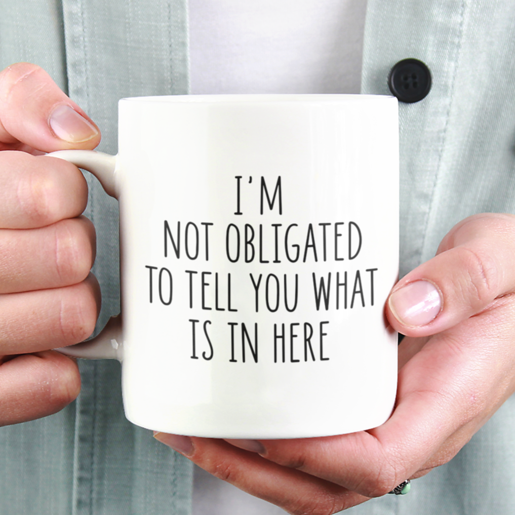 Simple yet impactful 11 oz white mug featuring the witty statement "I'M NOT OBLIGATED TO TELL YOU WHAT IS IN HERE" in a clear black font. Perfect for those with a dry wit and a desire for a bit of beverage privacy.