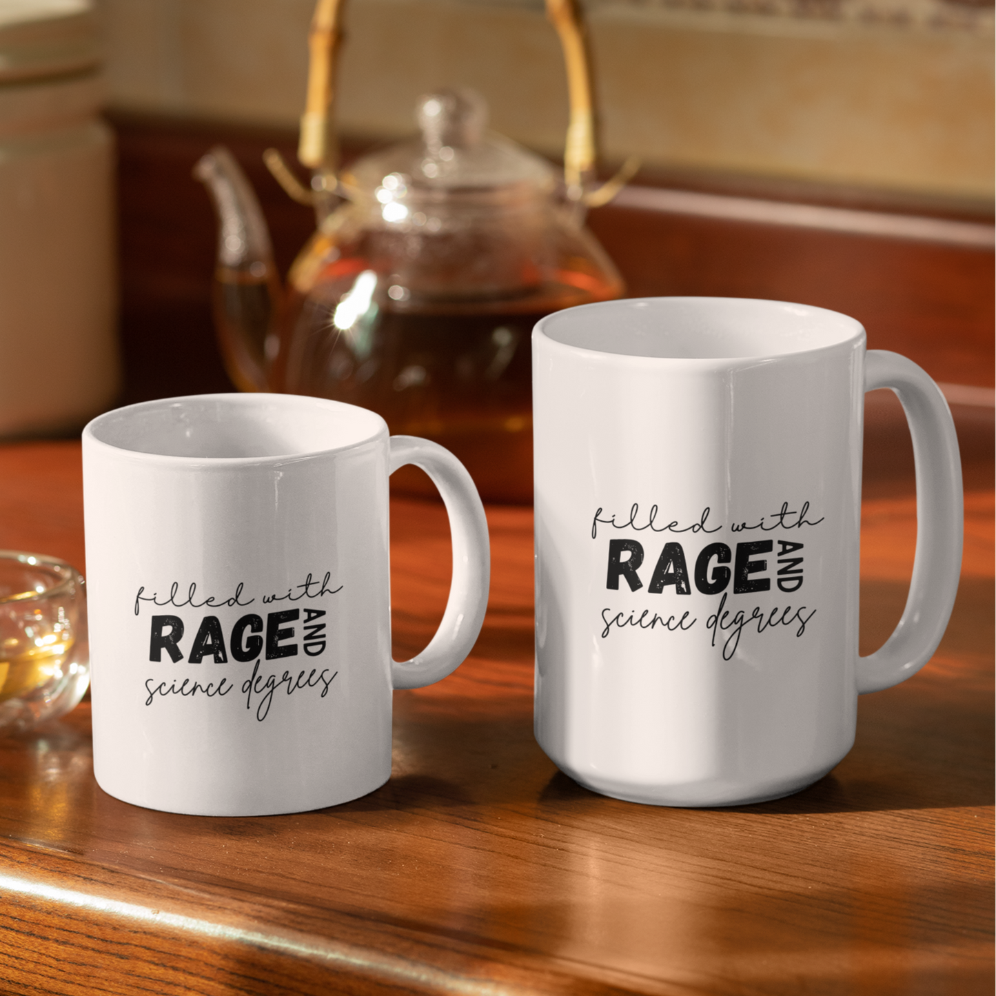 11 & 15 oz white mugs pictured on wooden table with black print reading 'filled with rage and science degrees'. Teapot pictured in background