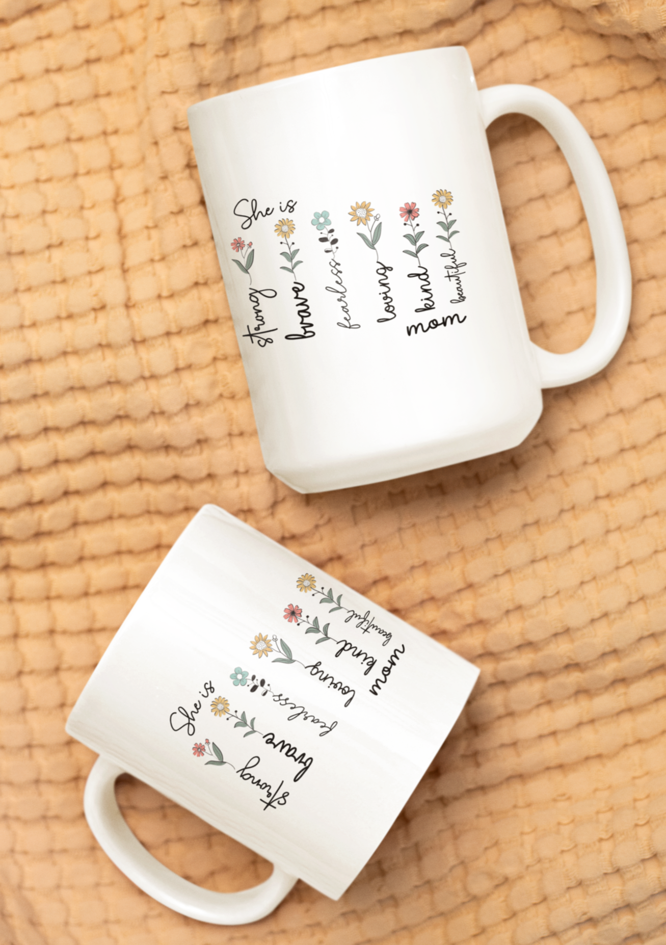 Elegant white ceramic coffee mug featuring a heartwarming floral design with the words “She is strong, brave, fearless, loving, kind, mom, beautiful” written alongside delicate illustrated flowers. The mug has a classic shape with a large, comfortable handle, making it both functional and beautiful. Displayed on top of stacked books with a pair of reading glasses nearby, the setting evokes a cozy, thoughtful vibe — perfect for gifting to moms, grandmothers, or inspirational women.