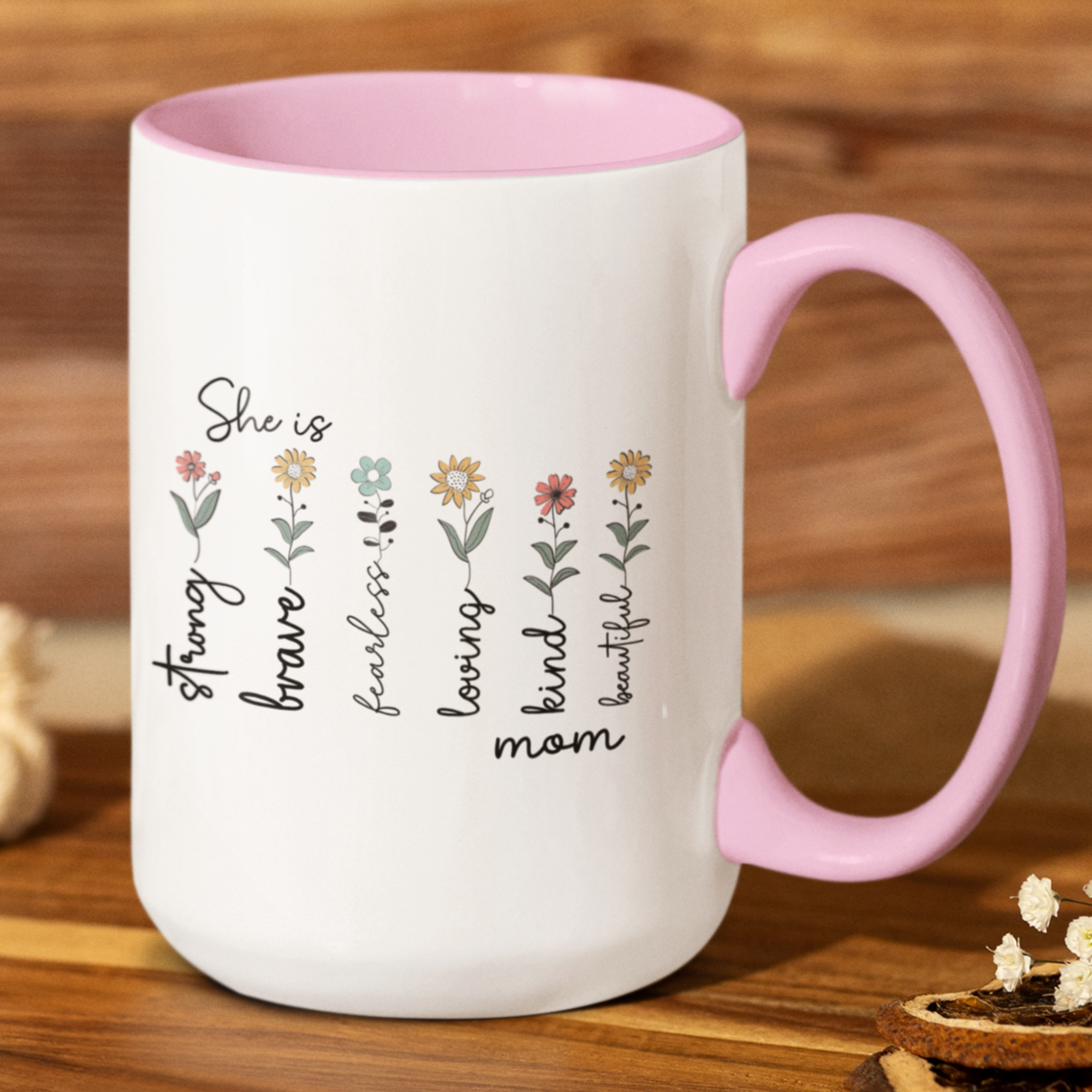 Charming 15 oz ceramic coffee mug with a glossy white exterior, soft pink interior, and matching pink handle. The design features delicate hand-drawn flowers paired with uplifting words that read: “She is strong, brave, fearless, loving, kind, mom, beautiful.” The heartfelt text and pastel floral accents create a warm, inspirational gift perfect for Mother's Day, birthdays, or everyday appreciation.