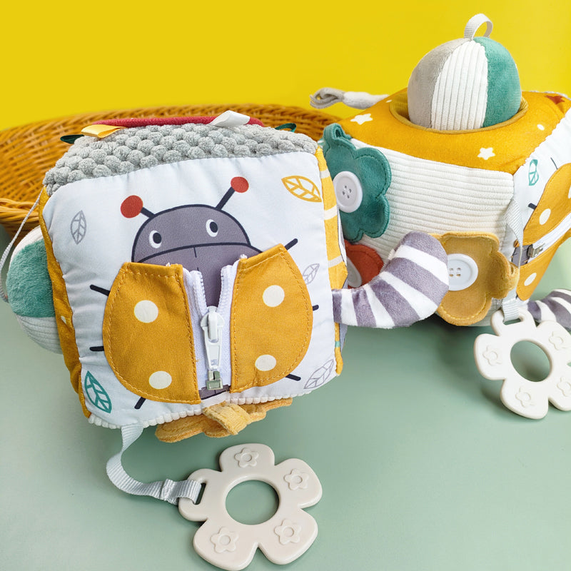 image of 2 plush activity blocks with multiple materials, buttons, zippers and teething rings. Color is gold, green and white
