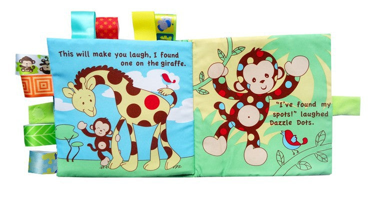 yellow plush book with monkey on front. title of book is "Dazzle Dots and the Missing Spots". Book also has multiple fabric sensory tags attached to the sides. Image is of interior pages with the book open