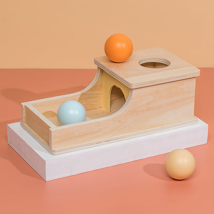 3 balls and wooden box with hole in top and arched exit into an open box