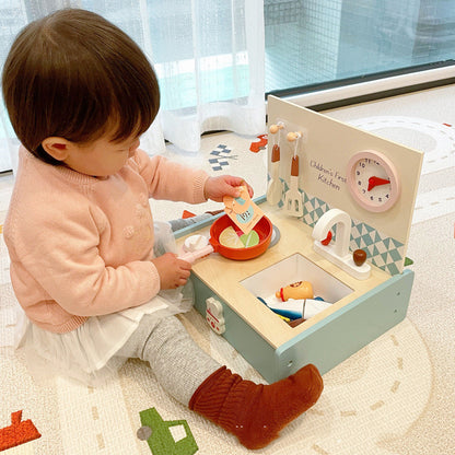 child playing with mini kitchen set putting something in a pan