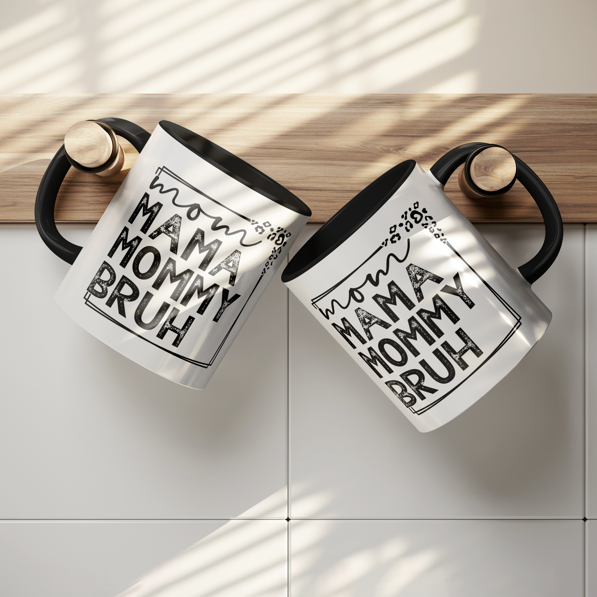 11 oz white ceramic mug with a black interior and handle. The mug features the black text "mom MAMA MOMMY BRUH" stacked vertically within a rectangular frame with leopard print accents. Dried citrus slices and small white flowers are arranged near the base of the mug.