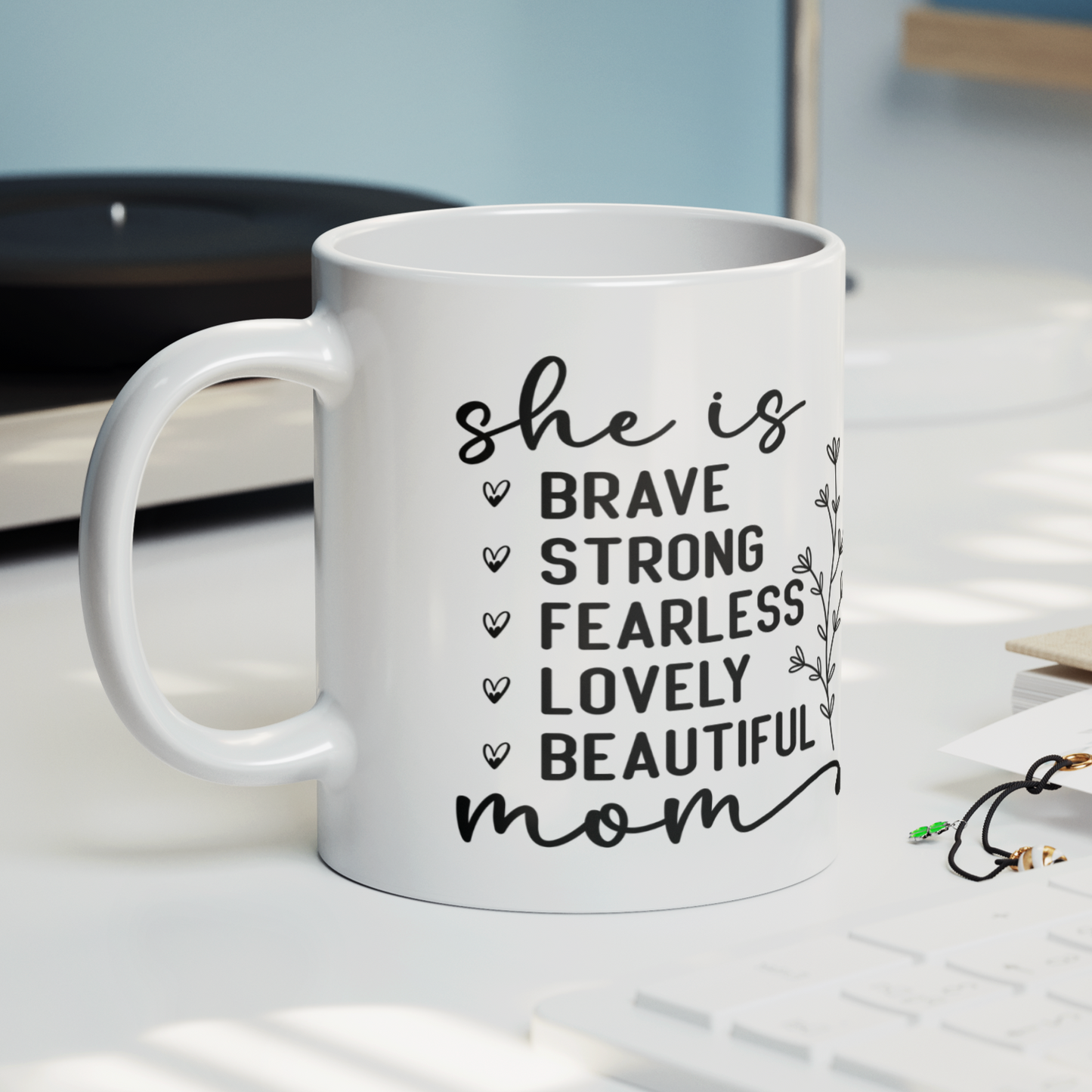 11 oz white mug displaying the empowering words 'she is BRAVE STRONG FEARLESS LOVELY BEAUTIFUL mom' in an elegant black font with a floral accent. A thoughtful gift for a mom.