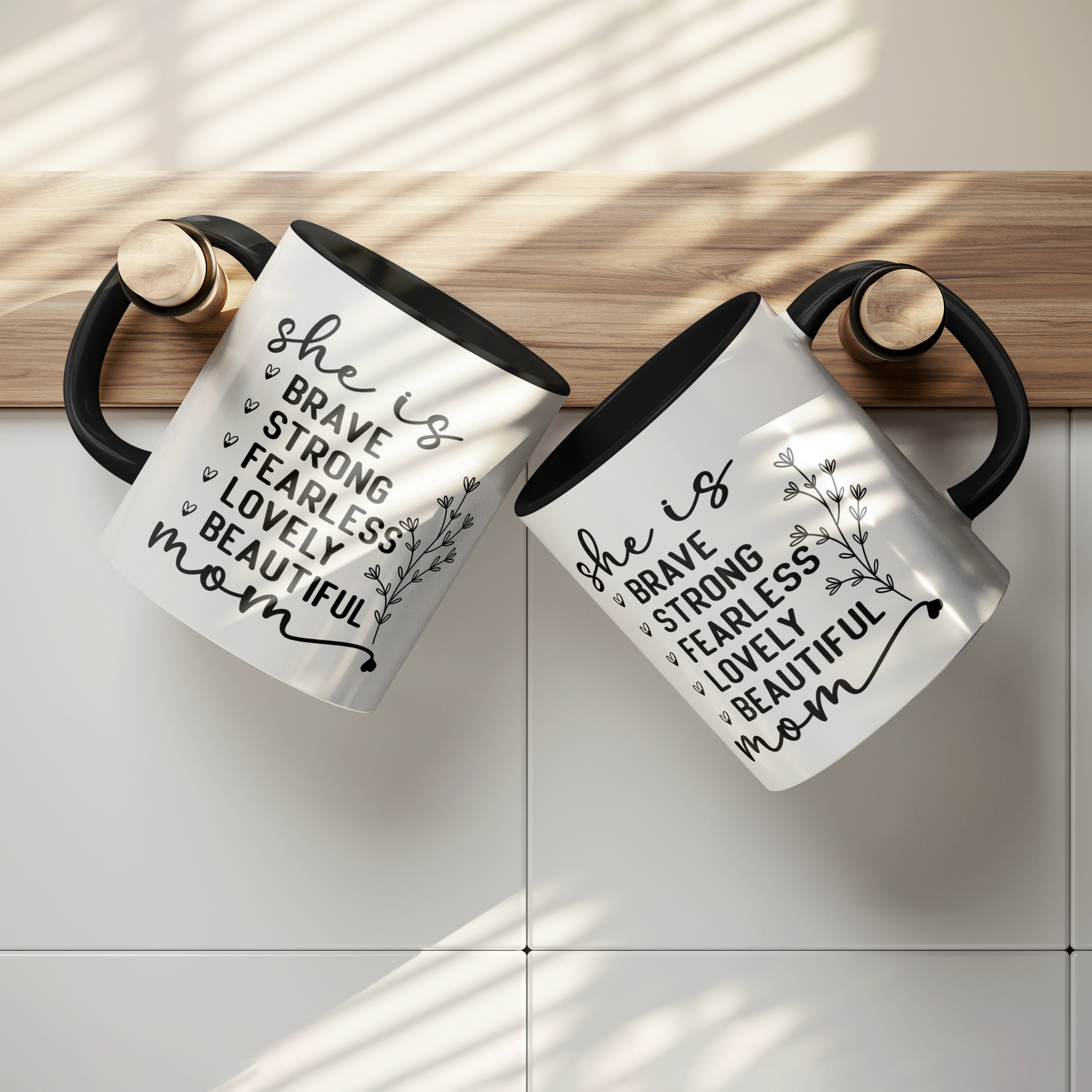11 oz white ceramic mug with a black interior and handle. The mug features the black text 'she is BRAVE STRONG FEARLESS LOVELY BEAUTIFUL mom' stacked vertically in a handwritten-style font, accompanied by a delicate floral illustration.