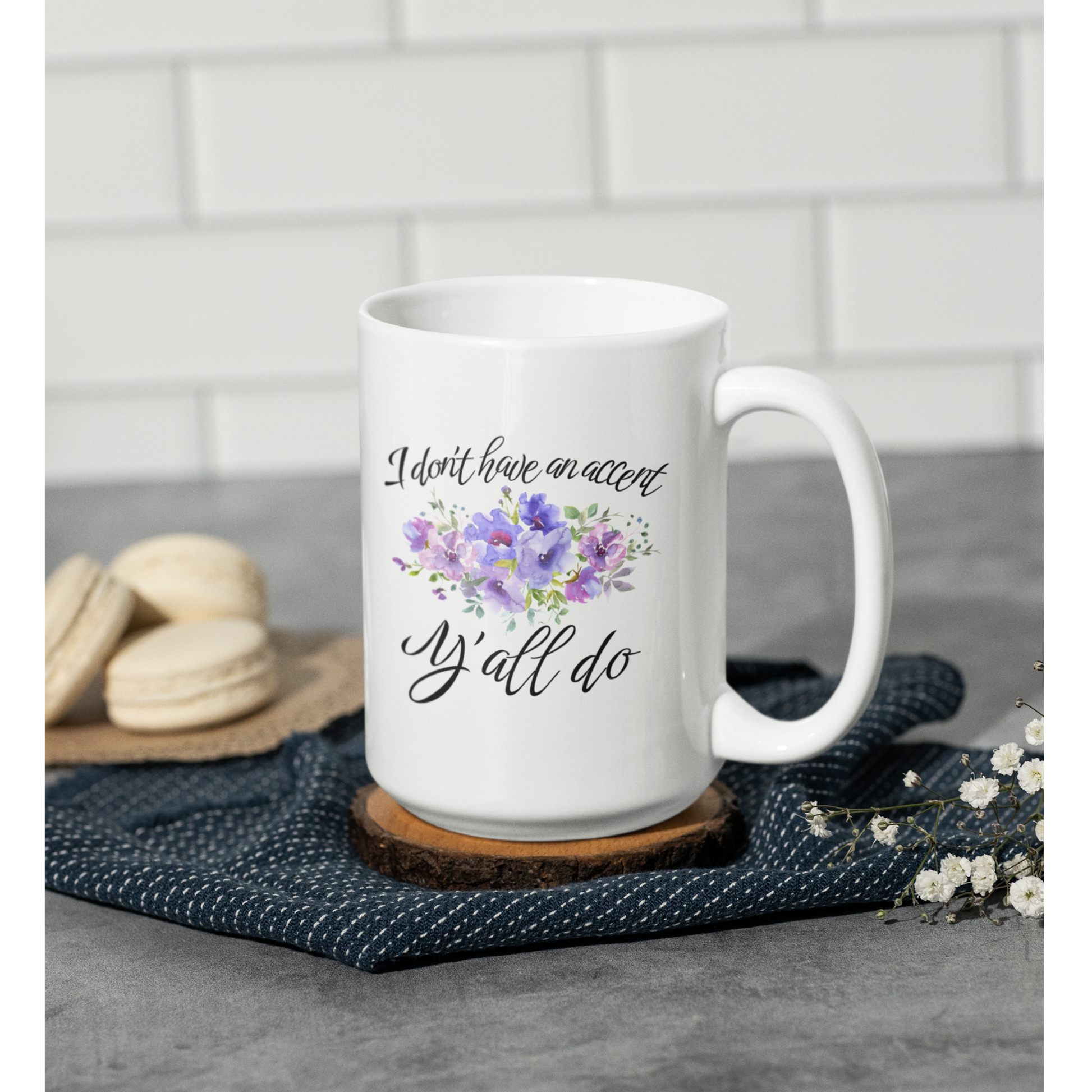 15 oz White ceramic coffee mug featuring a charming, southern-inspired design. The front showcases a whimsical quote in elegant, black cursive font that reads, “I don’t have an accent, Y’all do.” Between the two lines of text, there’s a delicate watercolor illustration of purple and lavender flowers with green foliage, adding a soft, feminine touch.