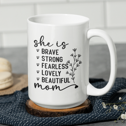 15 oz white mug displaying the empowering words 'she is BRAVE STRONG FEARLESS LOVELY BEAUTIFUL mom' in an elegant black font with a floral accent. A thoughtful gift for a mom.