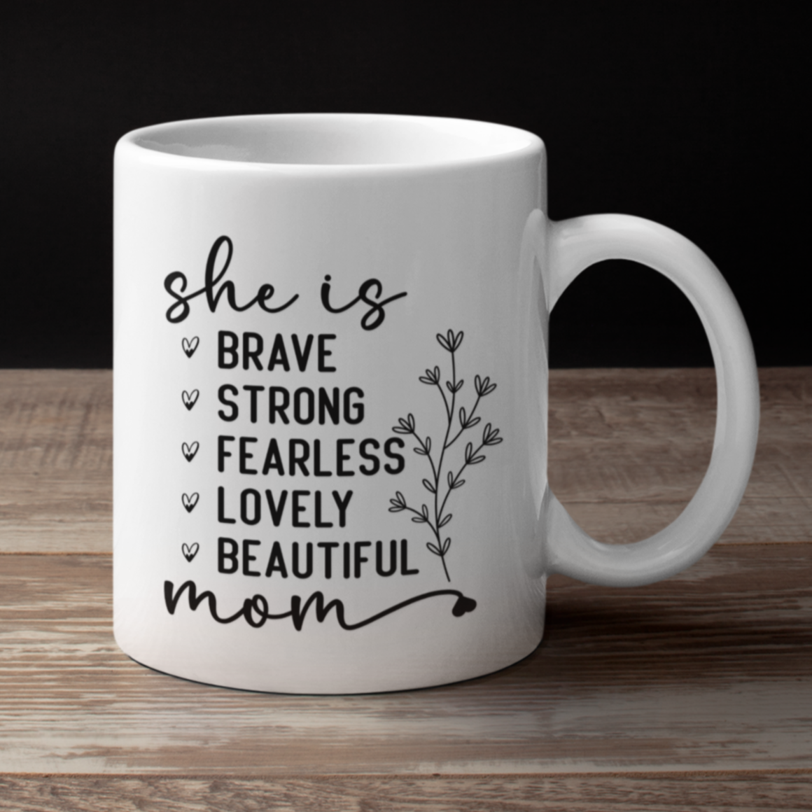 11 oz white mug displaying the empowering words 'she is BRAVE STRONG FEARLESS LOVELY BEAUTIFUL mom' in an elegant black font with a floral accent. A thoughtful gift for a mom.