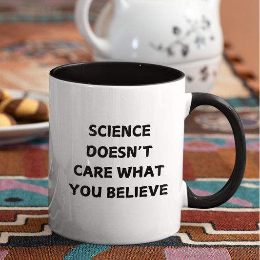 11 oz stylish ceramic coffee mug with a bold black handle and matching black interior, creating a sleek contrast against its glossy white exterior. The front of the mug features a powerful statement in all-capital black letters: "SCIENCE DOESN'T CARE WHAT YOU BELIEVE." The font is clean and impactful, making the message stand out.